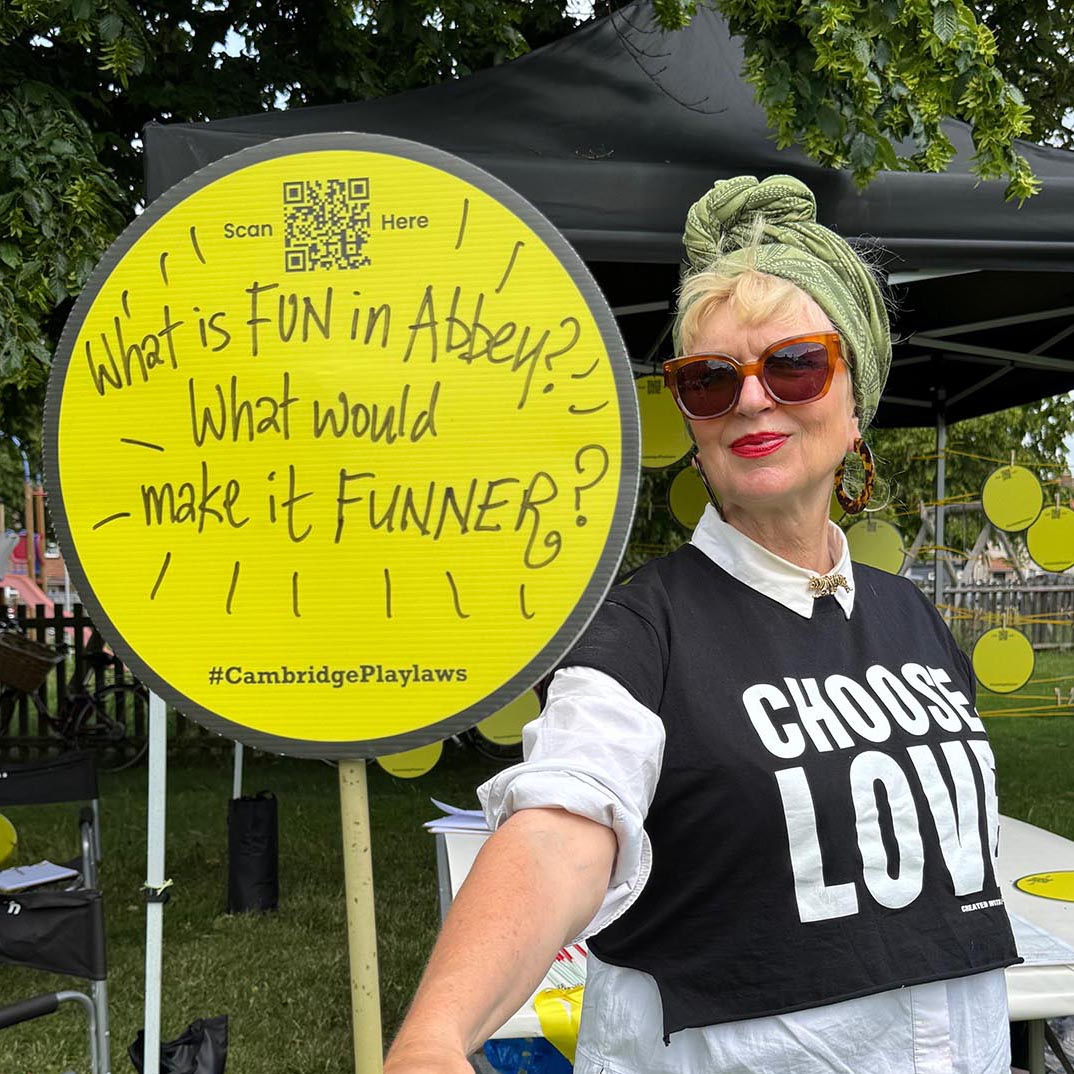 Hilary holding a hand drawn sign saying 'What makes Abbey FUN? What would make it FUNNER?'